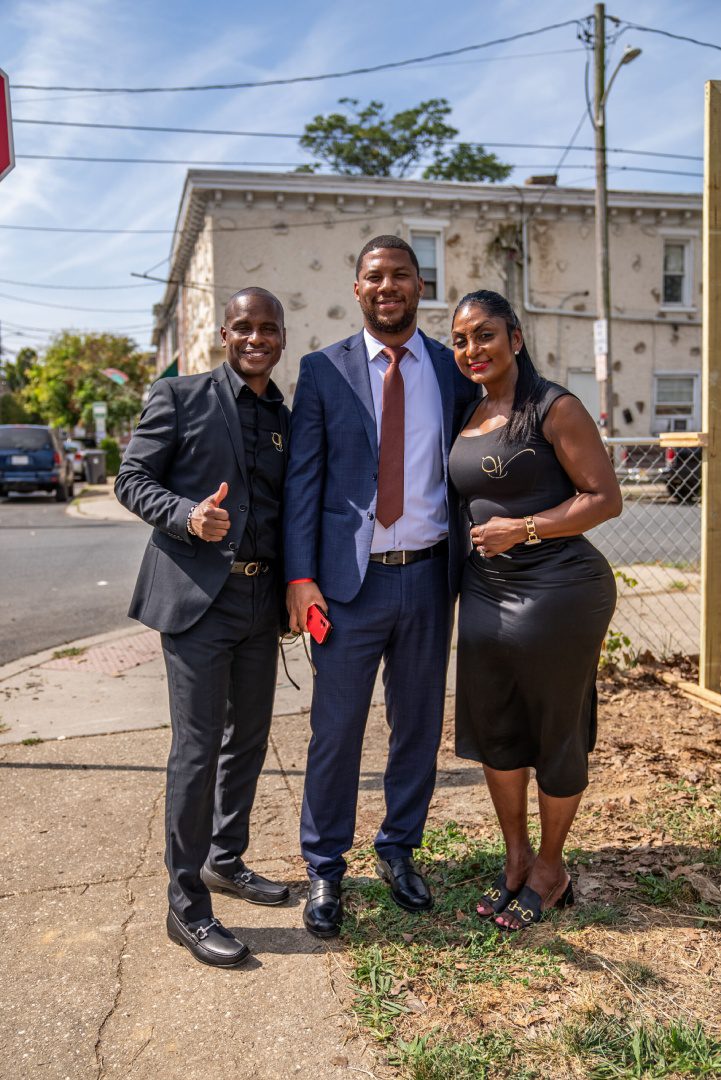 Three people standing on a sidewalk in front of a building.